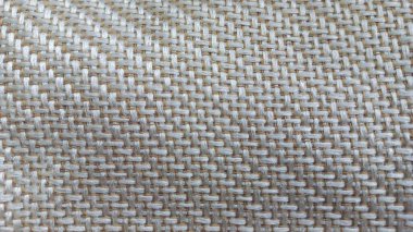 Örülmüş bir kumaşın detaylı bir yakın çekimi. Karmaşık iç içe geçmiş desenini nötr tonlarda gösteriyor.. 