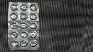 Siyah desenli yüzeyde boş bir hap kabarcığının görüntüsü. İlaç tüketimini veya sağlık hizmetlerini temsil eder.