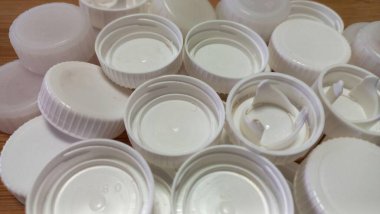 Tahta bir yüzey üzerinde gruplanmış beyaz plastik kapaklar koleksiyonu. Yeniden kullanımla ilgili geri dönüşümlü öğeler, organizasyon veya temaları temsil eder.