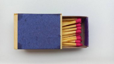 Koyu mavi kapaklı bir kibrit kutusunun yakın çekimi. Pembe uçlu ahşap kibritleri ortaya çıkarmak için kısmen açılmış. Düzenli düzenleme ve zıt renkler görsel olarak çekici bir kompozisyon oluşturur.