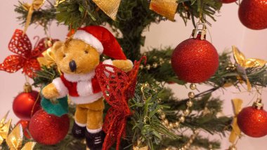 A beautifully decorated Christmas tree featuring a plush teddy bear ornament dressed as Santa, surrounded by red baubles, golden ribbons, and glittering butterflies, creating a warm holiday ambiance. clipart