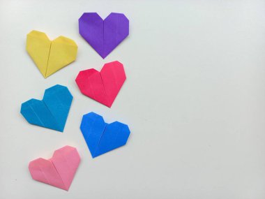 Sarı, mor, mavi, pembe ve kırmızı renkte altı canlı origami kalbi minimalist beyaz arka planda..