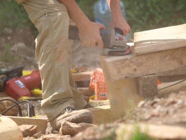 Elektrik öğütücüsüyle ahşap bir kalası zımparalayan bir işçinin yakın çekimi: Açık hava atölyesinde marangozluk ve zanaatkarlık gösteren bir sahne. Yüksek kalite fotoğraf