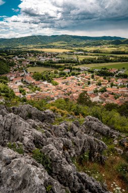 Kale Harabelerinden Vipava 'nın Resimli Manzarası: Kırmızılı Çatı ve Kilise Kulesi Önplanda Çiçek Açan Çiçekler ve Arka planda Yuvarlanan Tarlalar, Slovenya. 