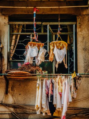 Hong Kong 'da Günlük Yaşam Sahnesi: Çamaşır asmak ve iç çamaşırları, yoğun bir şehir ortamında parmaklıklar ve perdelerle yıpranmış bir apartmanın penceresinin önünde kurutmak. Yüksek kalite fotoğraf