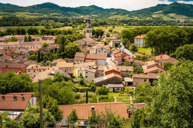Kale Harabelerinden Vipava 'nın resmi: Kırmızı döşemeli çatılar ve yeşil vadiye yerleştirilmiş Kilise Kulesi Ön planda Çiçekler ve Arka planda Yuvarlanan Tarlalar, Slovenya. Yüksek kalite