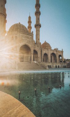 Azerbaycan 'ın Bakü kentindeki Heydar Camii, altın saatinde dört yüksek minaresi ve parlak mermer yüzeyine güzel yansıyan karmaşık taş işçiliğiyle yakalandı. Bu modern ama geleneksel İslam simgesi bir cultu sembolü olarak duruyor.