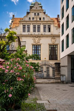 Münih 'teki Lenbachsplatz' daki tarihi bina dekoratif Gables, Stone Archway ve modern mimari, çiçek açan bitkiler ve bulutlu mavi gökyüzü ile çevrili kırmızı çatı. Yüksek kalite fotoğraf