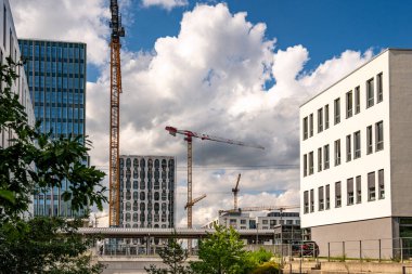 Freiham Münih 'teki Modern İnşaat Binası: Kemerli pencereleri, beyaz cepheleri, iskelesi ve canlı mavi gökyüzüne karşı bulutları ve şehirsel çevresi olan sütunları olan yüksek katlı bir bina. Yüksek kalite fotoğraf