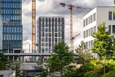 Freiham Münih 'teki Modern İnşaat Binası: Kemerli pencereleri, beyaz cepheleri, iskelesi ve canlı mavi gökyüzüne karşı bulutları ve şehirsel çevresi olan sütunları olan yüksek katlı bir bina. Yüksek kalite fotoğraf