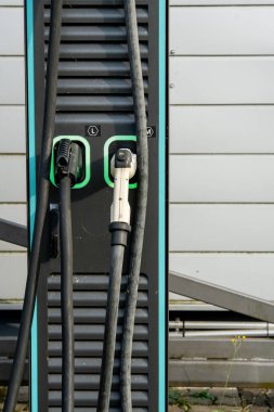 Çift bağlantıları olan elektrikli araç şarj istasyonu: Modern EV güç tedarik kablolarına yakın çekim ve şehir merkezinde üzerinde yeşil LED çizgileri olan prizler. Yüksek kalite fotoğraf