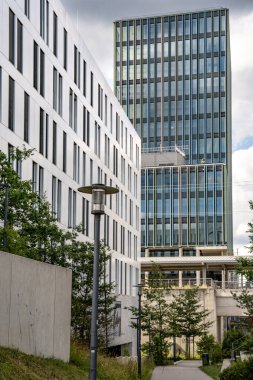 Freiham Münih 'teki Modern İnşaat Binası: Kemerli pencereleri, beyaz cepheleri, iskelesi ve canlı mavi gökyüzüne karşı bulutları ve şehirsel çevresi olan sütunları olan yüksek katlı bir bina. Yüksek kalite fotoğraf