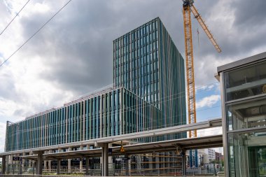 Freiham Münih Bavyera 'daki modern yüksek binalar kemerli cephe, modüler site konteynırları ve dramatik bulutlu gökyüzü altında çoklu sarı vinçler. Yüksek kalite fotoğraf