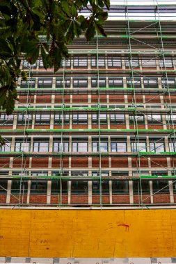 Münih 'teki Tarihi Bina Cephesi: Yeşil Metal İskelesi ve Eski Mimariyi Simetrik Pencereler ve Süslü Detaylarla çevreleyen Sarı İnşaat Bariyeri. Yüksek kalite fotoğraf
