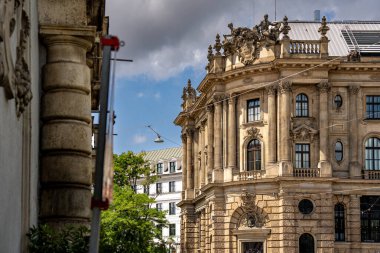 Münih 'teki Barok Mimari: Heykel Yüzlü Süslü Tarihi Bina, Kemerli Pencereler, Dekoratif Sütunlar ve Mavi Gökyüzü Altında Bulutlu Taş Detayları. Yüksek kalite fotoğraf