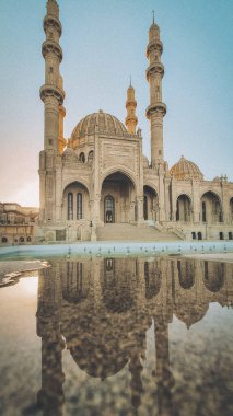Azerbaycan 'ın Bakü kentindeki Heydar Camii, altın saatinde dört yüksek minaresi ve parlak mermer yüzeyine güzel yansıyan karmaşık taş işçiliğiyle yakalandı. Bu modern ama geleneksel İslam simgesi bir cultu sembolü olarak duruyor.