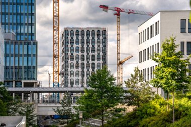 Freiham Münih 'teki Modern İnşaat Binası: Kemerli pencereleri, beyaz cepheleri, iskelesi ve canlı mavi gökyüzüne karşı bulutları ve şehirsel çevresi olan sütunları olan yüksek katlı bir bina. Yüksek kalite fotoğraf