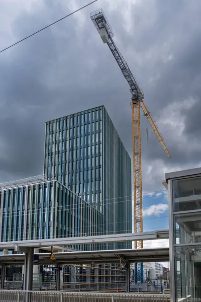 Freiham Münih Bavyera 'daki modern yüksek binalar kemerli cephe, modüler site konteynırları ve dramatik bulutlu gökyüzü altında çoklu sarı vinçler. Yüksek kalite fotoğraf