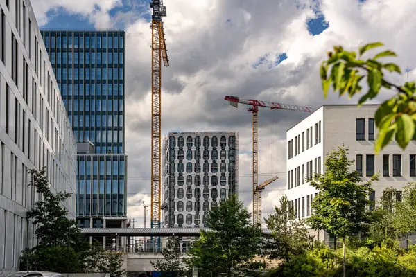 Freiham Münih 'teki Modern İnşaat Binası: Kemerli pencereleri, beyaz cepheleri, iskelesi ve canlı mavi gökyüzüne karşı bulutları ve şehirsel çevresi olan sütunları olan yüksek katlı bir bina. Yüksek kalite fotoğraf