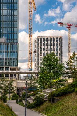 Freiham Münih 'teki Modern İnşaat Binası: Kemerli pencereleri, beyaz cepheleri, iskelesi ve canlı mavi gökyüzüne karşı bulutları ve şehirsel çevresi olan sütunları olan yüksek katlı bir bina. Yüksek kalite fotoğraf