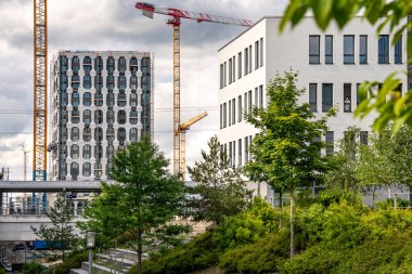 Freiham Münih 'teki Modern İnşaat Binası: Kemerli pencereleri, beyaz cepheleri, iskelesi ve canlı mavi gökyüzüne karşı bulutları ve şehirsel çevresi olan sütunları olan yüksek katlı bir bina. Yüksek kalite fotoğraf