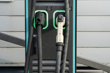 Çift bağlantıları olan elektrikli araç şarj istasyonu: Modern EV güç tedarik kablolarına yakın çekim ve şehir merkezinde üzerinde yeşil LED çizgileri olan prizler. Yüksek kalite fotoğraf