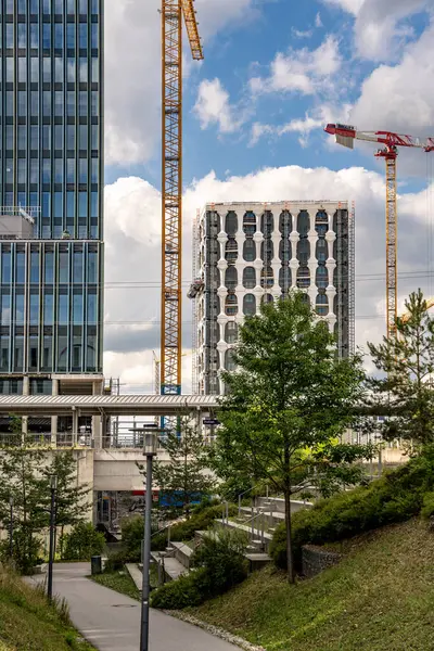 Freiham Münih 'teki Modern İnşaat Binası: Kemerli pencereleri, beyaz cepheleri, iskelesi ve canlı mavi gökyüzüne karşı bulutları ve şehirsel çevresi olan sütunları olan yüksek katlı bir bina. Yüksek kalite fotoğraf