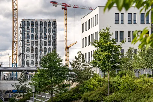 Freiham Münih 'teki Modern İnşaat Binası: Kemerli pencereleri, beyaz cepheleri, iskelesi ve canlı mavi gökyüzüne karşı bulutları ve şehirsel çevresi olan sütunları olan yüksek katlı bir bina. Yüksek kalite fotoğraf