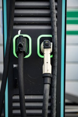 Çift bağlantıları olan elektrikli araç şarj istasyonu: Modern EV güç tedarik kablolarına yakın çekim ve şehir merkezinde üzerinde yeşil LED çizgileri olan prizler. Yüksek kalite fotoğraf