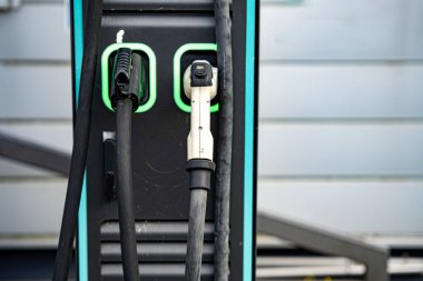 Çift bağlantıları olan elektrikli araç şarj istasyonu: Modern EV güç tedarik kablolarına yakın çekim ve şehir merkezinde üzerinde yeşil LED çizgileri olan prizler. Yüksek kalite fotoğraf