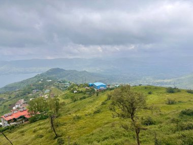 Üzerinde binalar olan dağlar, bir nehir ve bulutlu gökyüzü. 