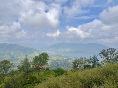 Çimenler ve ağaçlar, kırmızı çatılı bir bina, bir nehir ve dağlar. 