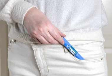 Beyaz elbiseli kadının elinde şeker hastaları ve kilo kaybı için mavi bir Ozempic enjeksiyon kalemi var.