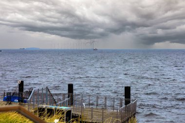 Bulutlu havada deniz manzarası Gri bulutlar ve uzakta yel değirmenleri