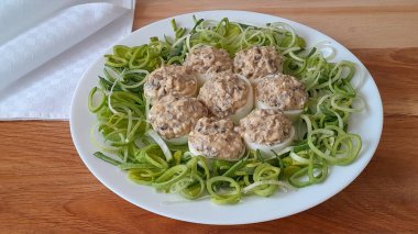 the art of food, stuffed eggs, eggs with onions on white plate, leeks on the kitchen table 