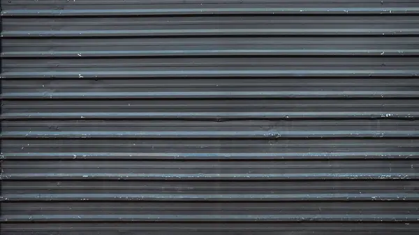 Paralel oyukları ve çıkıntıları gösteren kıvrımlı metal bir levhanın yakın görüntüsü, hafif aşınma ve yıpranma izleri var. Metal yüzey ışığı yansıtarak endüstriyel bir estetik oluşturur..