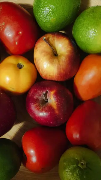Elmalar, domatesler ve limonlar da dahil olmak üzere çeşitli taze meyvelerin doğal ışık altında canlı bir görüntüsü..