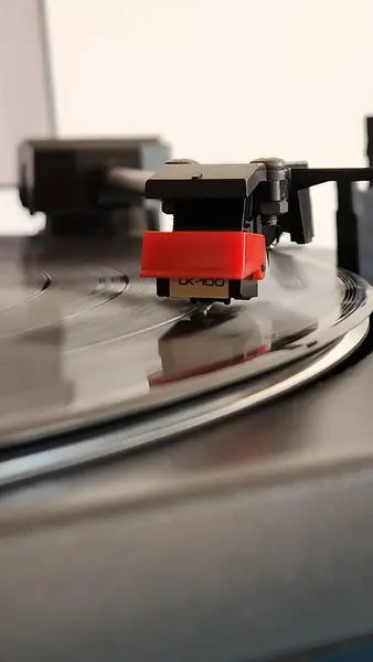 Siyah bir plak plağı boyunca hareket eden bir turntable iğnesinin yakın plan görüntüsü, analog müzik üretiminde nostaljik ve klasik özü, kanallara odaklanmış bir şekilde yakalıyor..