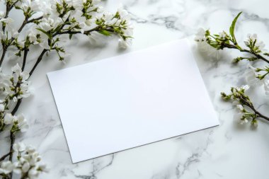 Mermer bir yüzeye yerleştirilmiş, beyaz çiçeklerle çevrili boş bir kartın maketi. Zarif ve minimalist tasarımlar için mükemmel. Görüntü AI tarafından oluşturuldu.