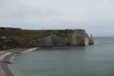 Etretat 'ın beyaz kayalıkları bulutlu bir gökyüzünün altında neredeyse durgun görünüyor, sert kıştan eser yok..