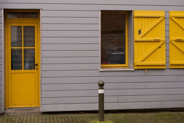 Canlı sarı kapısı ve uyumlu panjurları olan eşsiz gri bir duvar, görünüşüne neşe katıyor.