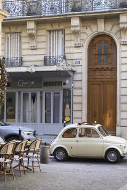 Eski bir klasik araba, şık kafeterya sandalyeleri ve zarif mimarisi olan büyüleyici ve antika bir Paris caddesi.