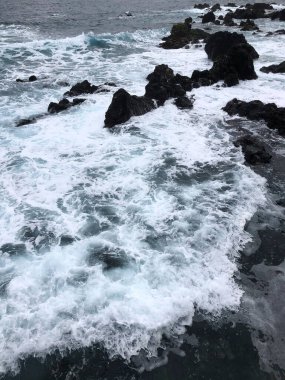Dinamik okyanus dalgaları fırtınalı bir sahil şeridinde engebeli kayalara şiddetle çarparak inanılmaz dramatik bir manzara yaratıyor.