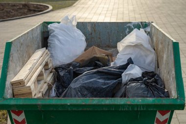 Ahşap kalaslar, plastik çöp torbaları ve kağıt atıkları da dahil olmak üzere inşaat atıklarıyla dolu yeşil endüstriyel çöp konteynırlarına yakın çekim.