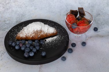 Lezzetli tatlı kompozisyonu taze tereyağlı kruvasan tozlu pudra şekeri ve yanında koyu çikolata parçalı bir bardak dut şerbeti.