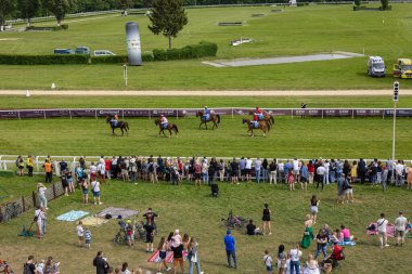 Wroclaw, Poland- Maj 3, 2024: Güneşli bir günde yarış pistinde at binicilerini izleyen izleyiciler, aile dostu bir atmosferi kuşattı.