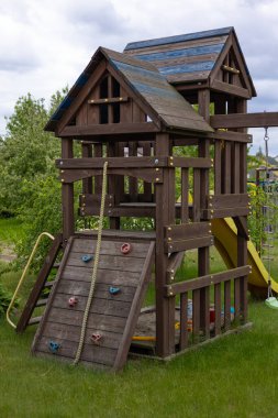 Bulutlu bir günde duvarına, ipine tırmanan ve arka bahçeye kayan ahşap çocuk parkı güvenli bir ortamda çocuklar için aktif oyun, yaratıcılık ve fiziksel gelişimi teşvik ediyor.