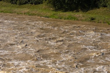 Nehir kenarındaki güçlü çalkantılı su. Şiddetli yağmurun neden olduğu güçlü bir akıntı. Çalkantılı çamurlu su hızla akar ve doğanın gücünü gösteren yoğun dalgalar yaratır.