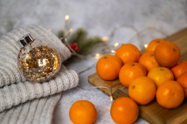 Festive arrangement with fresh tangerines on a wooden board surrounded by glowing Christmas lights and a golden glitter ornament. Holiday warmth, seasonal fruits and festive decor clipart