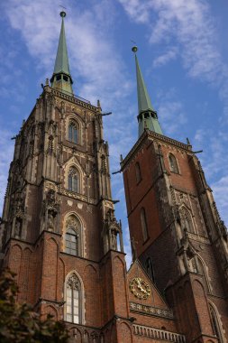 Polonya 'daki Wroclaw Katedrali' nin Gotik tarzı ikiz kuleleri mavi gökyüzünün altında, sivri kemerler ve karmaşık heykellerle süslü mimariler sergileniyor.